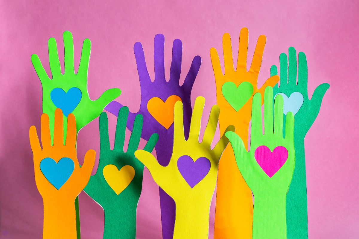 Multi-colored paper hands against a pink background. They all have different colored hearts on their palms.