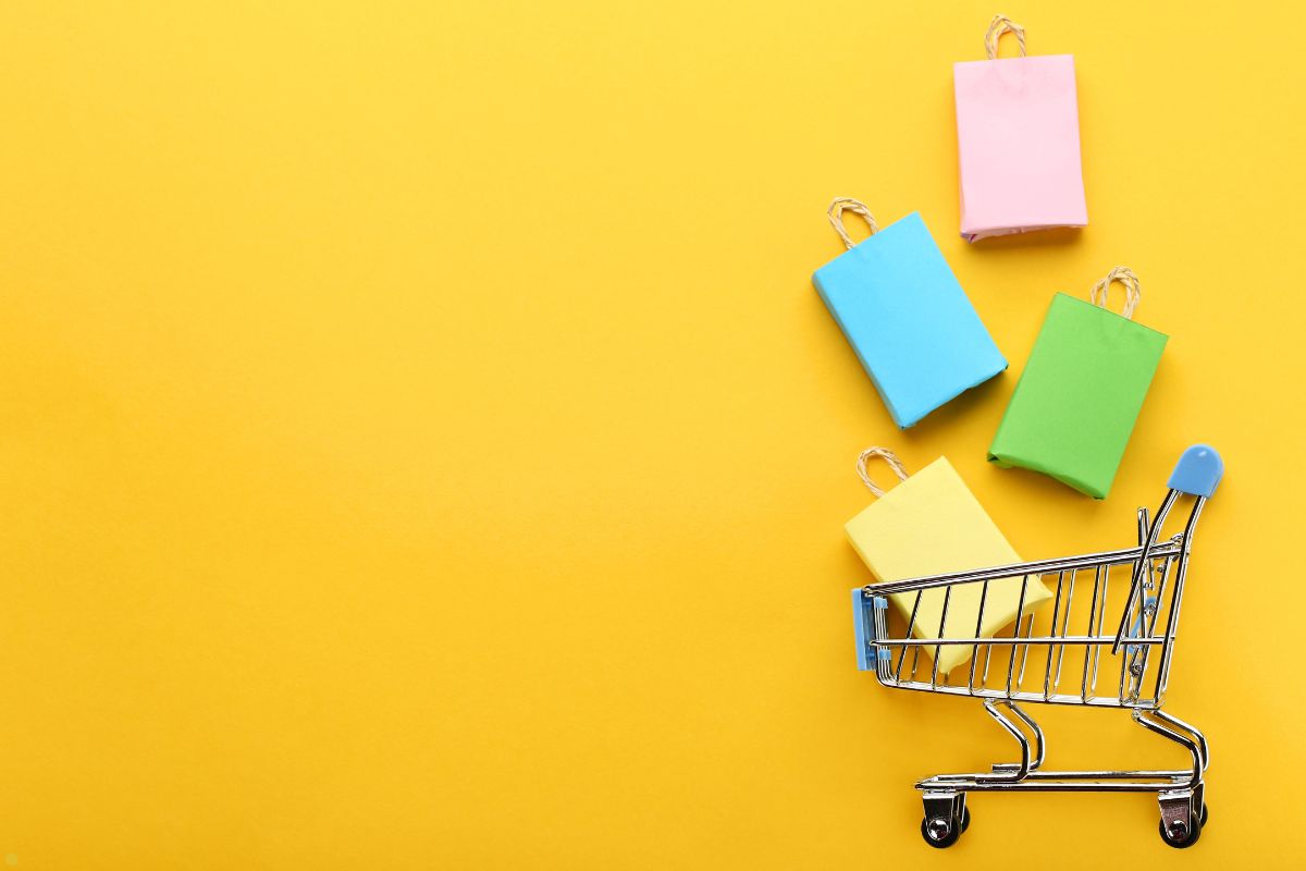 A shopping cart with colorful bags coming out of it on a yellow background.